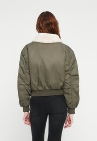 Maslinasto zelena bomber jakna s bijelim krznom na ovratniku, rebrastim manžetama i donjim rubom, s nabranim rukavima i glatkom, teksturiranom tkaninom.