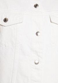 Camicia in denim bianco con design strutturato, due tasche sul petto, bottoni automatici argentati e texture liscia con cuciture tonali sottili.