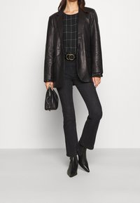 Svart läderblazer med en strukturerad design, ihop med en svart och vit rutmönstrad topp, högmidjade svarta jeans och svarta spetsiga stövlar.