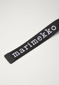 Black fabric strap with white "marimekko" text. Smooth texture, rectangular shape, and prominent branding feature without additional embellishments.