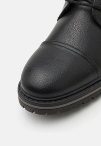 Svart skinnstøvel med teksturert overflate, rund tå og svart gummisåle med rillede detaljer. Glatte sømmer langs det øverste.