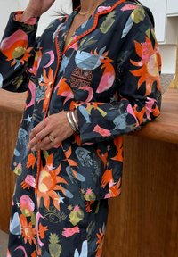 Värvikas pidžaama komplekt, millel on julged lille- ja abstraktsed mustrid oranžis, roosas, sinises ja rohelises tumedal taustal. Unikaalsed õmblusdetailid.