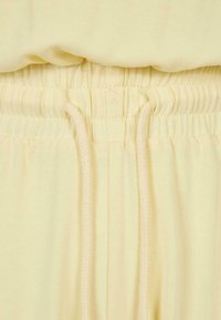 Pantalon jaune clair à cordon de serrage avec une taille élastique, en coton doux et à la texture lisse. Les cordons de serrage sont bien visibles.