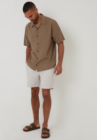 Brun kortærmet button-up skjorte med sorte knapper, parret med hvide shorts og brune hjemmesandaler. Glat stof, afslappet pasform.