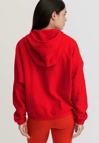 Felpa rossa con una consistenza morbida, cappuccio e maniche lunghe, abbinata a leggings rossi coordinati. La felpa ha una vestibilità rilassata e orlo a costine.