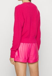 Sweter z dzianiny w kolorze fuksji o luźnym kroju, z szerokimi rękawami i fakturowaną tkaniną. Do tego błyszczące szorty w kolorze fuksji z podwiniętym brzegiem.
