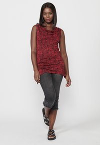 Top sans manches à motifs floraux rouges avec un décolleté drapé, associé à un jean cropped foncé avec des coutures décoratives et des sandales noires.