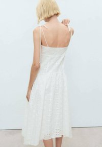 Abito in cotone bianco con motivo a occhiello, design senza maniche e spalline regolabili. Silhouette svasata che arriva a metà polpaccio.