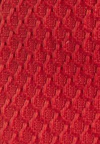 Strukturierter roter Stoff mit einem gewebten Muster, das kleine Quadrate und erhabene Akzente zeigt und ein taktiles, filigranes Erscheinungsbild bietet.