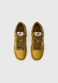 Nike tenisice u gorućoj žutoj boji, s gornjim dijelom od suede i kože, okrugli vrh, perforirani detalji i tamnosmeđe vezice. Bijela gumena potplat.