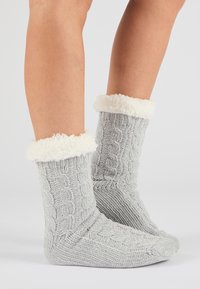 Calcetines tejidos grises con un patrón acanalado, que cuentan con un puño de piel sintética blanca. Textura suave y diseño hasta el tobillo, adecuados para uso en interiores.