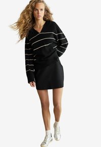 Sort sweater med hvide striber, v-hals, parret med en sort mini-skjorte og sølv sneakers. Tekstureret stof med ribbede detaljer.