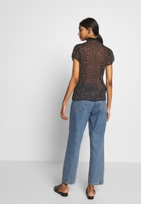 Blusa nera trasparente con maniche a sbuffo, piccoli pois bianchi, design aderente, abbinata a jeans in denim blu chiaro a gamba dritta.