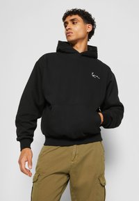 Sweatshirt à capuche noir en coton, avec une poche kangourou et un petit logo blanc sur la poitrine. Poignets et ourlet côtelés.