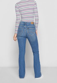 Niebieskie dżinsy z wysokim stanem i rozszerzanymi nogawkami, wykonane z dżinsu. Posiadają detale w postaci przeszyć oraz dwie tylne kieszenie. Widoczna jest brązowa skórzana metka z logo marki.