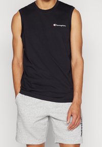 Svart ärmlös tröja i bomull med en liten röd och vit Champion-logga på bröstet; matchad med grå shorts.