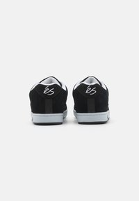 Sorte suedette sneakers med hvite detaljer, med polstret krage, flat gummisåle og en fremtredende logo på hælkappen.
