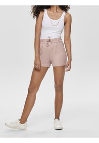 Light pink shorts made of a smooth fabric, featuring a tie waistband, pleats at the front, and side pockets. Worn with a white tank and sneakers.