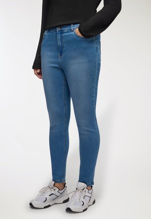 Jeans skinny in denim blu medio con texture liscia, vita alta e tasche frontali angolate. Abbinati a sneaker bianche e nere.
