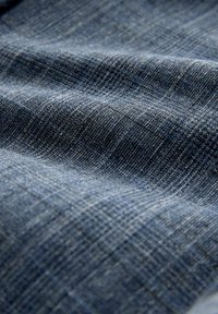 Strukturierter blauer Stoff mit verschiedenen Schattierungen, einem dezenten Karomuster und einem weichen Gewebe, das Tiefe und visuelles Interesse schafft.