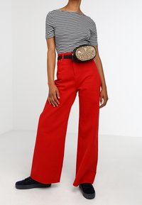 Czerwone spodnie z szerokimi nogawkami, czarno-biała bluzka w paski na krótki rękaw oraz nerka w panterkę. Modelka nosi czarne trampki.