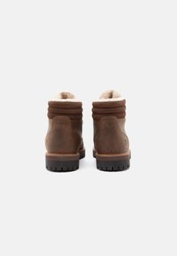 Pair of brown leather winter boots with padded collar and shearling lining, shown from the back on a white background.