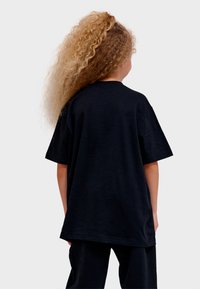 Svart bomulls-t-shirt med avslappnad passform, korta ärmar och rund halsringning. Synliga sömnadsdetaljer nära fållen.