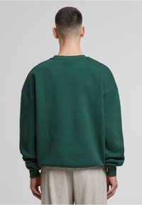 Felpa verde con una vestibilità comoda, spalle basse e polsini a costine. Realizzata in un tessuto morbido, presenta una superficie pulita e liscia.