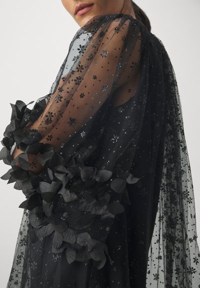 Rochie neagră din material transparent, cu broderie florală, mâneci volan și accente din dantelă. Materialul transparent pune în evidență detalii și designuri intricate.