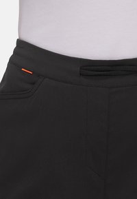 Schwarze Hose mit glatter Textur, featuring eine Vordertasche, einem dezenten orangen Akzent und einem elastischen Bund.