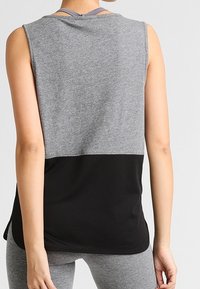 Woman wearing sleeveless gray and black sports top with gray leggings, shown from the back against a plain background.