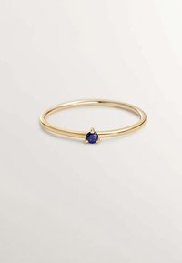 Anillo de oro con una banda circular y lisa y una pequeña piedra de zafiro redonda engastada en un ajuste de cuatro garras en el centro.
