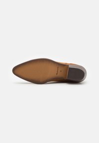Suola di scarpa in pelle marrone con forma appuntita. Presenta una texture rigata e una sezione del tacco più scura in contrasto. Logo del marchio visibile.