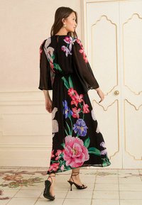 Čierne maxi šaty s kvetinovým vzorom a dlhými, priehľadnými rukávmi. Obsahujú živé vzory kvetov v ružovej, modrej a zelenej farbe. Elastický pás, vzdušný strih.
