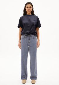 Marineblaue Satinbluse mit kurzen Ärmeln und einem Tie an der Taille, kombiniert mit ausgebleichten blauen High-Waist- weit geschnittenen Jeans und beigen Slippern.