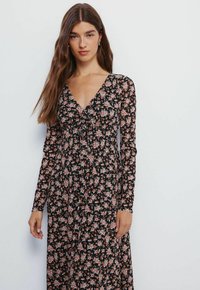 Sort langærmet kjole med et blomsterprint i pink og hvid. V-udskæring, blomsterprint, flydende stof og knælang design.