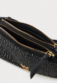 Geantă de mână neagră cu o suprafață texturată, având trei compartimente cu fermoar, accesorii aurii și un accent din curea de piele.