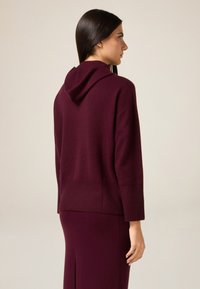 Kapturowa bluza w kolorze bordo z prążkowaną teksturą na dole i mankietach. Luźny krój, rękawy o długości do połowy ramienia oraz miękki, lekki materiał.