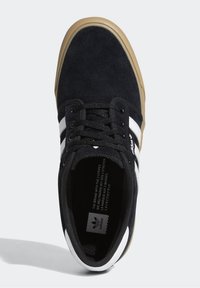 Svart mockaskor med vita tre ränder, snörningsdesign, svarta snören, gummigummiyttersula och synligt varumärke inuti.