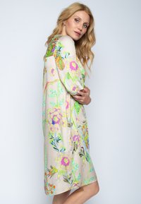 Blumenkleid aus leicht beigem Stoff mit lebhaften rosa, grünen und blauen Mustern. Lockere Passform mit Dreiviertelärmeln und knie-langer Schnittform.