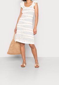 Abito bianco lavorato a maglia con strisce azzurro chiaro, texture a coste e spalline in pizzo; abbinato a una borsa a tracolla intrecciata e sandali.