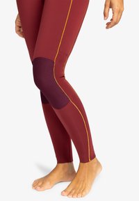 Maroon leggings with yellow stitching, ribbed texture at the knee, stretchy fit, and ankle-length design. Feet visible without shoes.