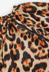 Tkanina s leopardím vzorem zahrnuje odstíny oranžové, černé a béžové s texturovaným designem. Obsahuje řadu dekoračních stehování podél švu.