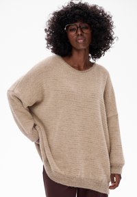Beżowy oversize sweter z okrągłym dekoltem, teksturowanym materiałem i opadającymi ramionami. Posiada boczne rozcięcia dla swobody ruchów.