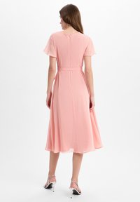 Roze chiffon jurk met korte fladdermouwen, een aansluitende taille en een vloeiende rok, voorzien van een discreet rits achteraan en een bijpassende riem. Zilveren hakken.