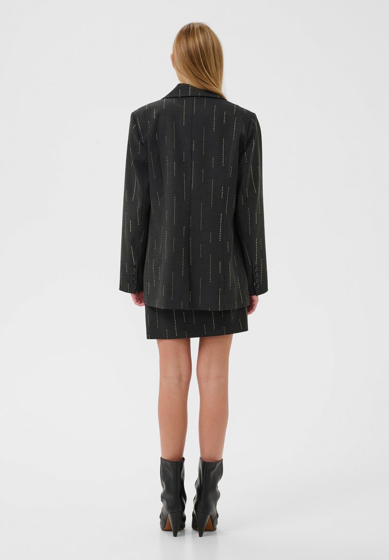 Completo giacca e gonna nera con un motivo a righe verticali, tessuto testurizzato, maniche lunghe e stivaletti neri alla caviglia.