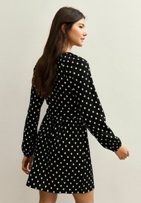 Vestido negro con mangas largas, patrón de diamantes blancos, cintura entallada y falda acampanada. Tejido texturizado con un ligero brillo.