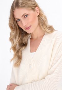 Cardigan a coste di colore crema con maniche lunghe e scollatura a V profonda, caratterizzato da due grandi bottoni e un motivo testurizzato su tutto il tessuto.