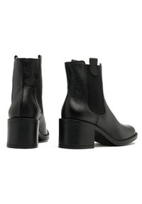 Bottes courtes en cuir noir avec une finition texturée, des panneaux latéraux élastiques et un talon bloc. Le design comprend une languette à l'arrière.