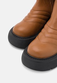 Bruna läderankelboots med rund tå, texturerad yta, ribbad svart gummisula och stickade detaljer över överdelen.